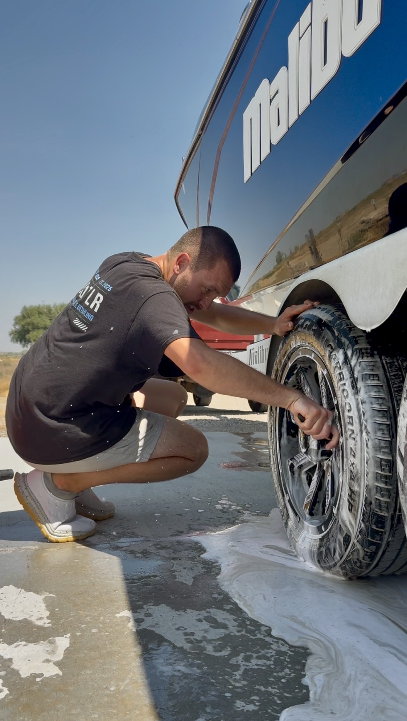 PRO DTLR detailer hand-washing a wheel on a boat trailer with foam and a detailing brush